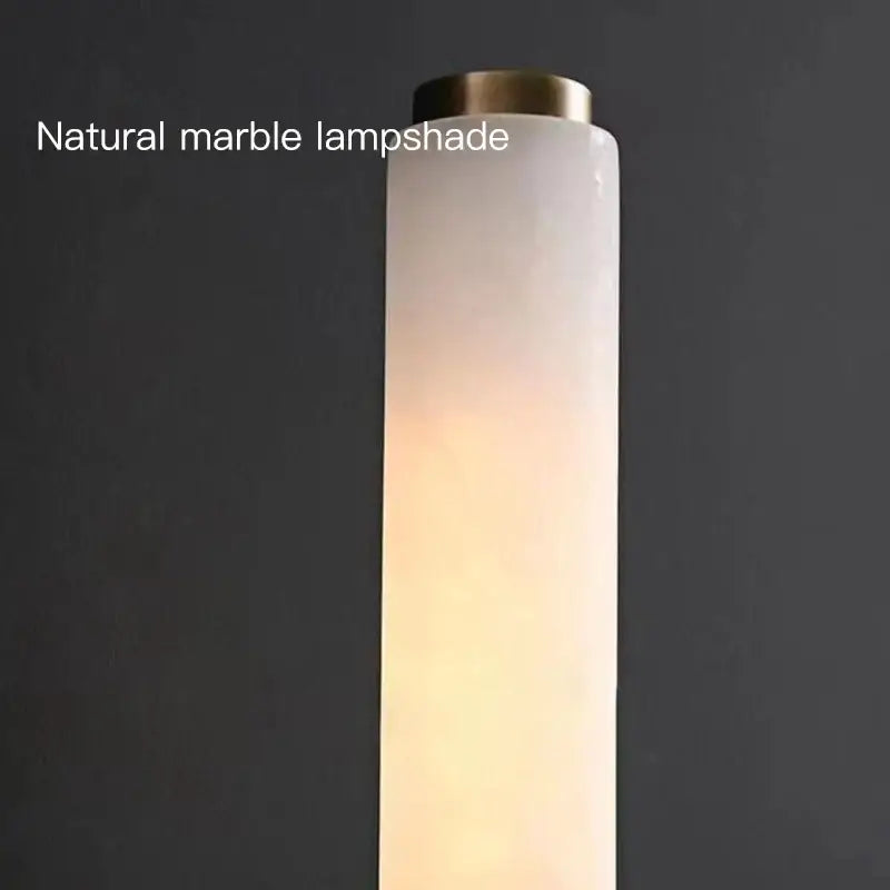 Elegant marble copper wall sconce with a tall cylindrical natural marble lampshade and brass-finished top for bedroom lighting