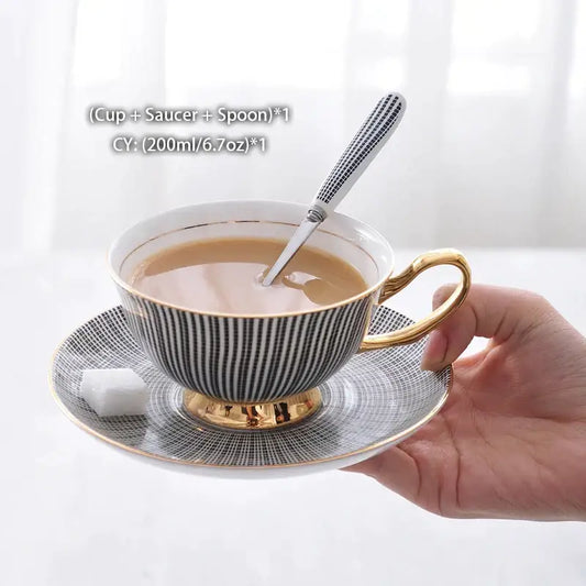 Elegant black and white striped porcelain tea cup set with gold trim held in hand with matching saucer and spoon