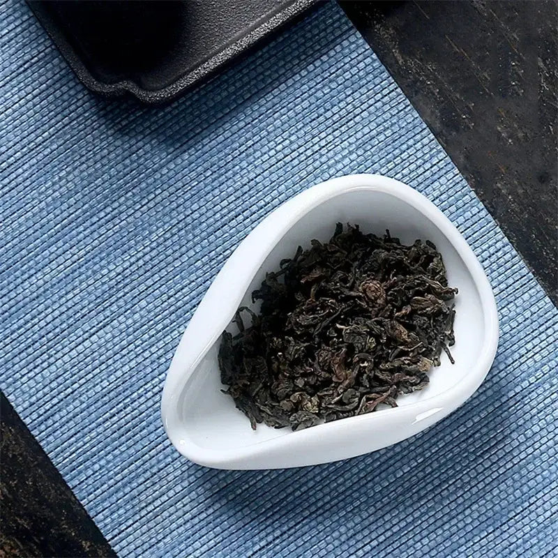 A white ceramic dose tray filled with dark tea leaves from decorbites ceramic white tea spoon set for kitchen use