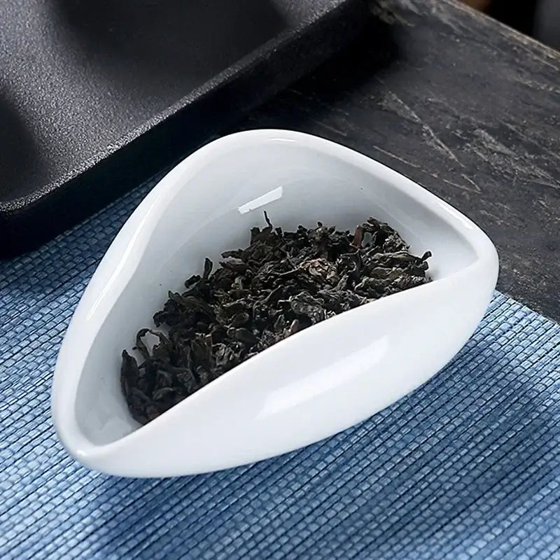 A sleek white ceramic dose tray with a tea spoon filled with dark curly loose-leaf tea decorbites ceramic white