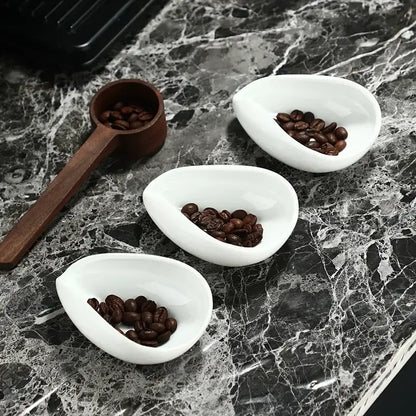 Elegant white ceramic dose trays with dark roasted coffee beans and a tea spoon from decorbites ceramic white set