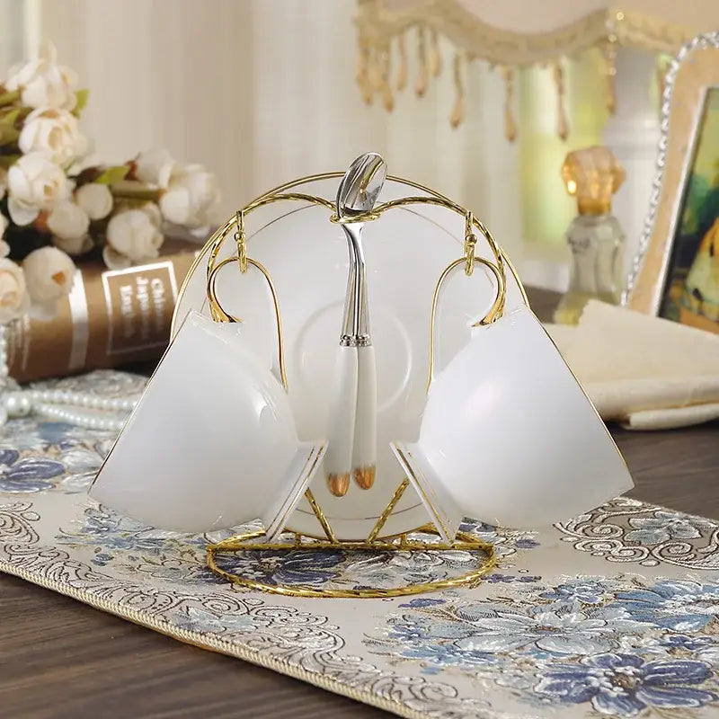 Elegant white and gold bone china coffee set with porcelain teacups and saucers displayed on a decorative stand