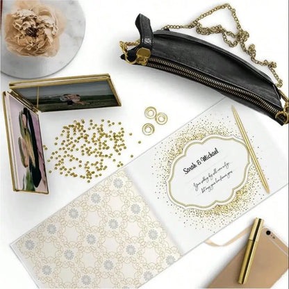 Black leather crossbody pouch with gold-tone zipper and chain strap alongside elegant white decorbites guest book with bronzing detail