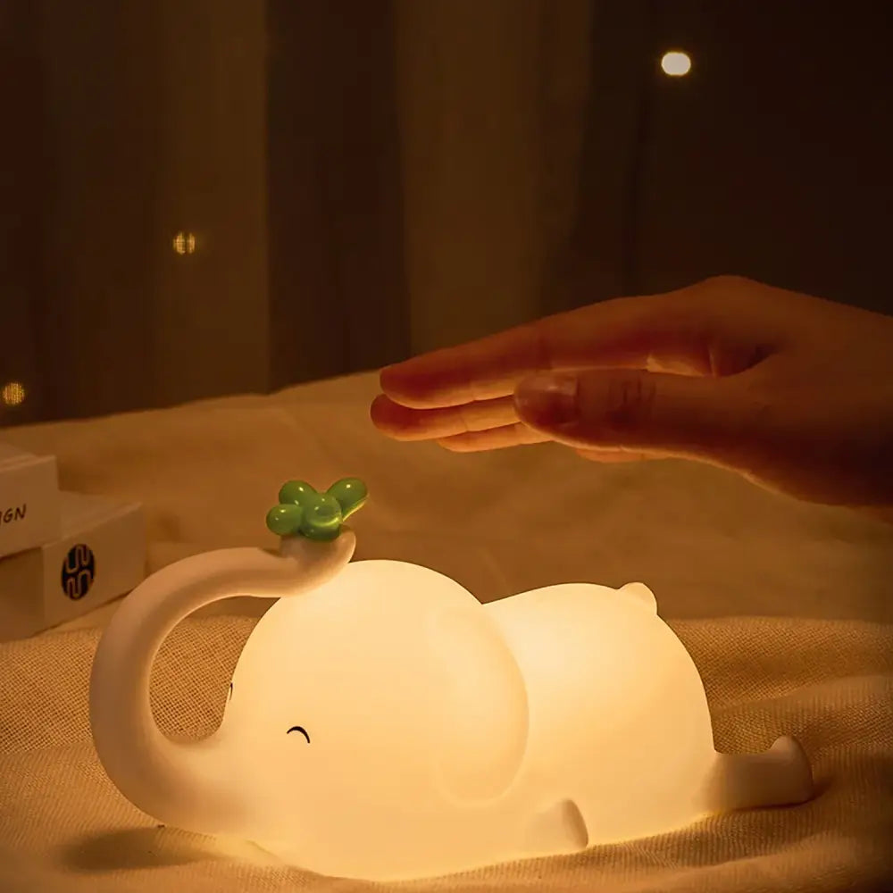A soft glowing white decorbites elephant silicone night light with a green four-leaf clover on its trunk for bedroom decor