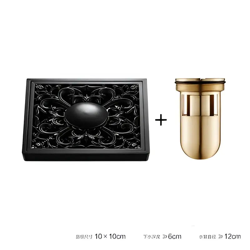 Black ornate brass square floor drain with embossed floral design and gold-toned cylindrical drain cover for shower room