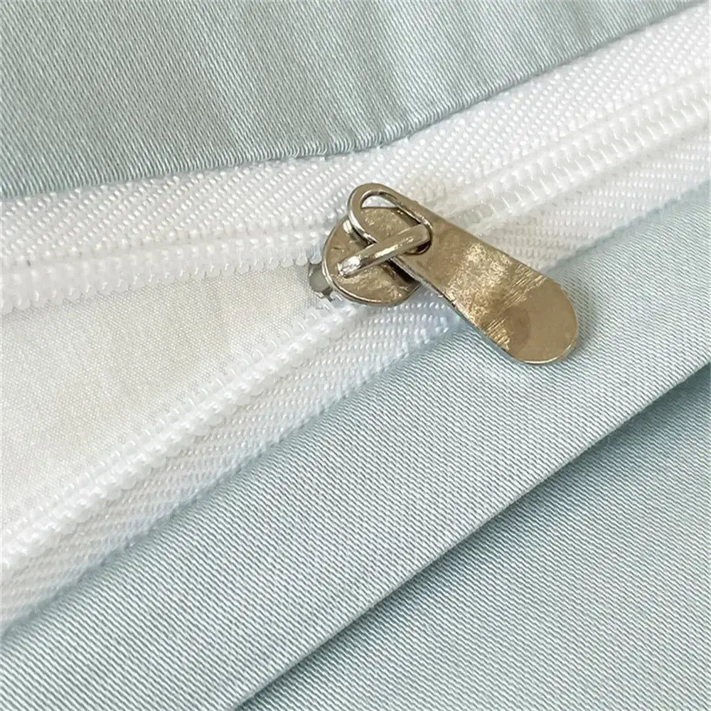 A metallic gold-toned zipper pull on a white track against light blue satin fabric of an embroidered egyptian cotton duvet cover set