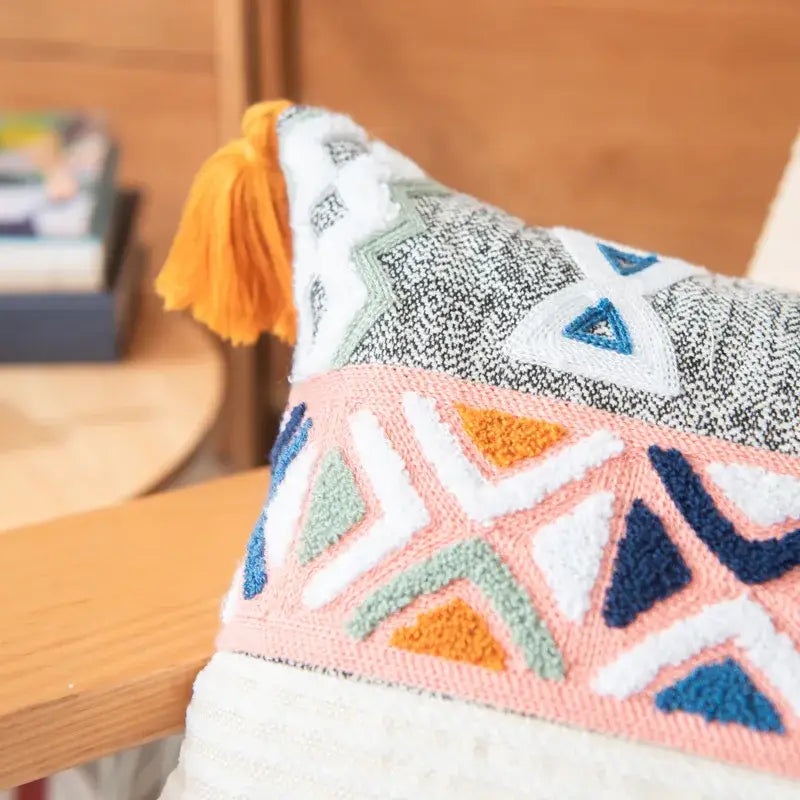 A cozy embroidered blue tufted pillow cover with vibrant geometric pattern and orange tassel for boho decorbites decor