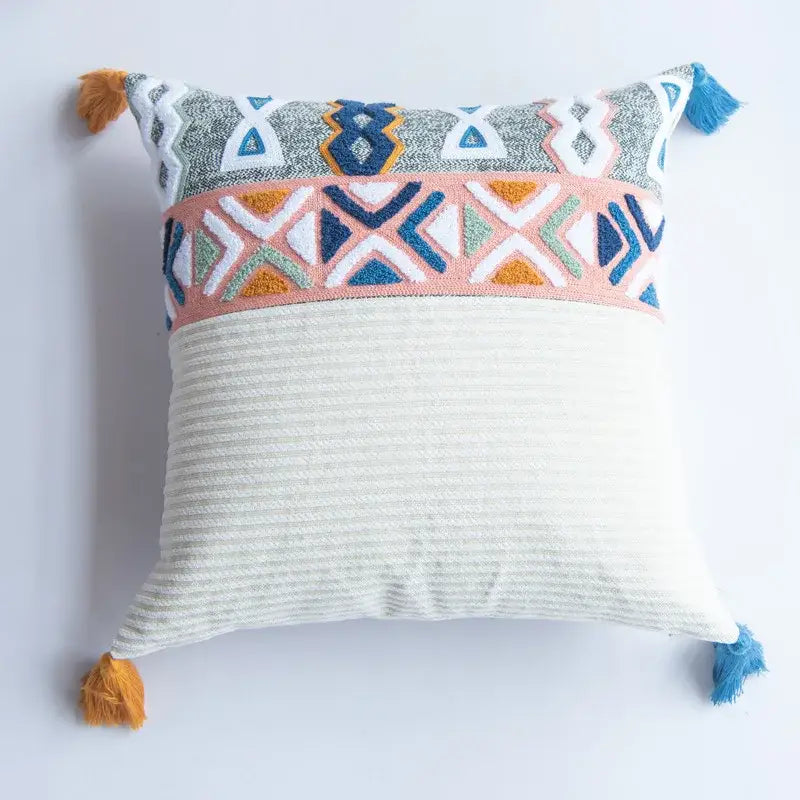 A square pillow cover with an off-white ribbed base and decorbites embroidered blue tufted geometric patterns and tassels