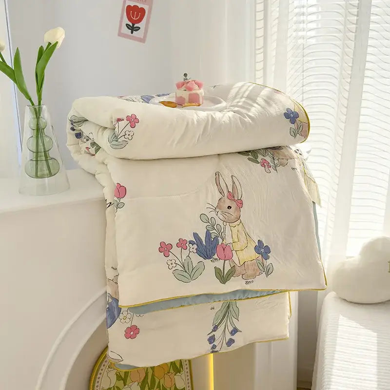 A soft cream-colored double gauze rabbit print quilt featuring an embroidered bunny in a yellow dress with floral accents