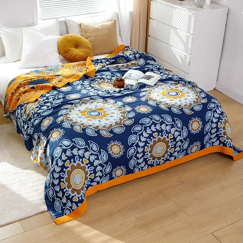 A cozy navy blue decorbites cotton gauze throw blanket with embroidered white gold and orange floral pattern and orange border