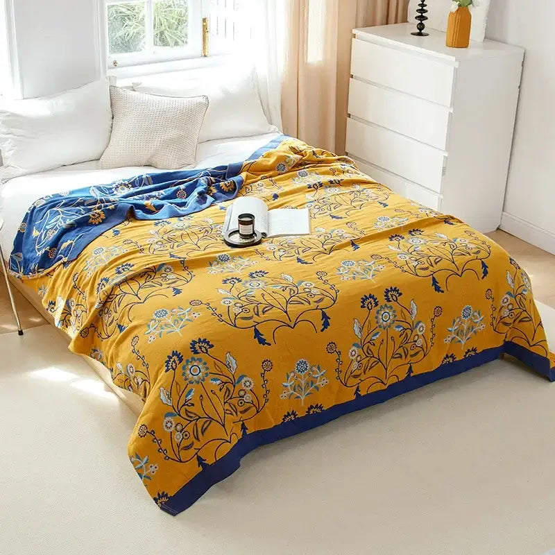 Vibrant yellow floral throw blanket with navy blue border and intricate patterns draped over bed made of decorbites cotton gauze