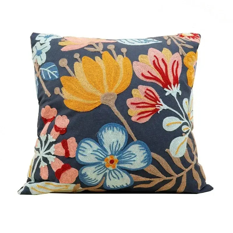 A square cushion cover with dark navy fabric and vibrant embroidered flower boho design in yellow pink red and blue hues