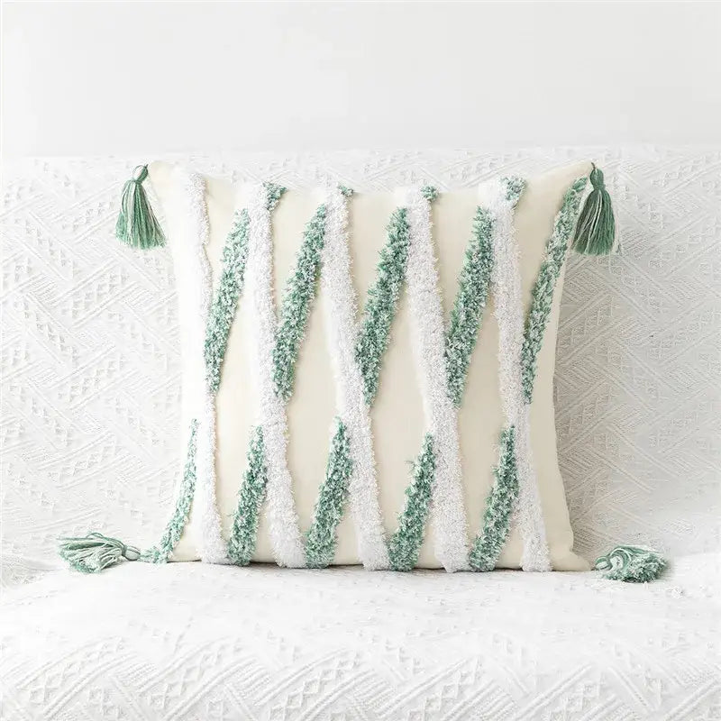 Cream-colored pillow cover with embroidered geometric leaves featuring green and white textured yarn stripes and tasseled corners