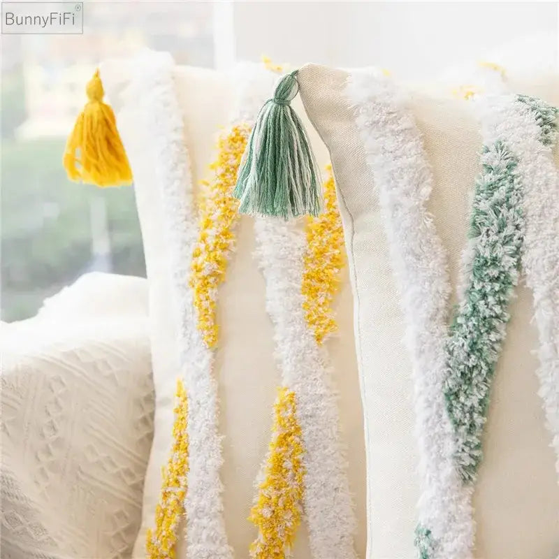 Cream-colored pillow cover with embroidered geometric leaves featuring white yellow and green yarn stripes and tassels