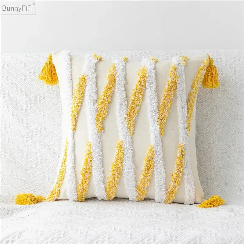 Cream-colored pillow cover with embroidered geometric leaves design and textured white and yellow tasseled accents
