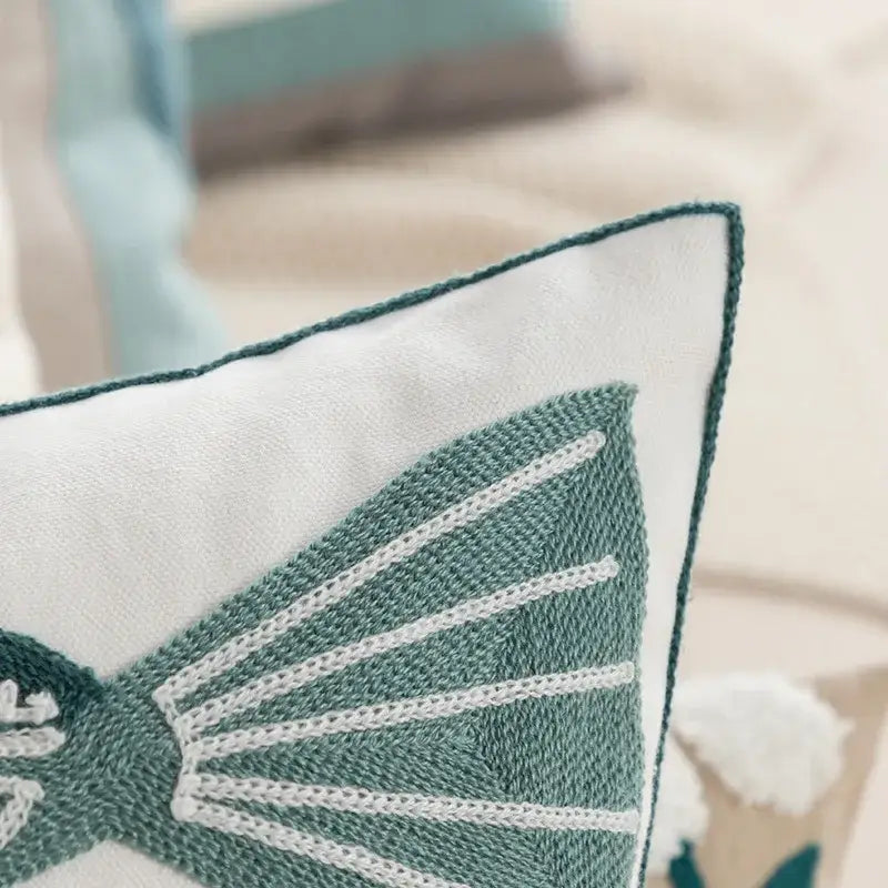 A white pillow cover with teal embroidered butterfly and white stitching complementing daisy yellow floral decor