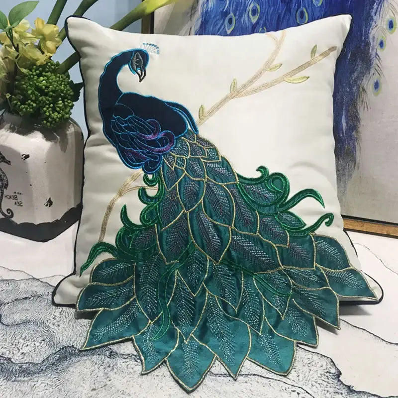 Cream satin cushion cover featuring an embroidered peacock design in deep teal navy blue with gold thread detailing