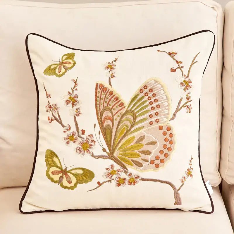 Cream-colored embroidered cushion cover with intricate butterfly and blossom designs in green brown and orange for sofa