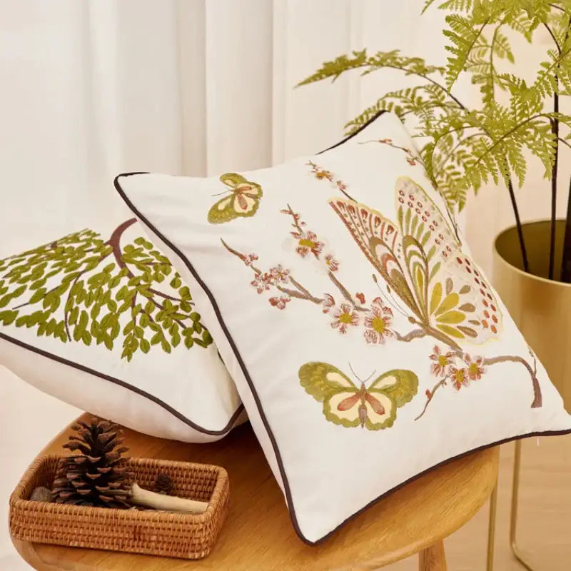 White embroidered cushion cover with butterflies and blossoms in green brown and pink hues for living room sofa
