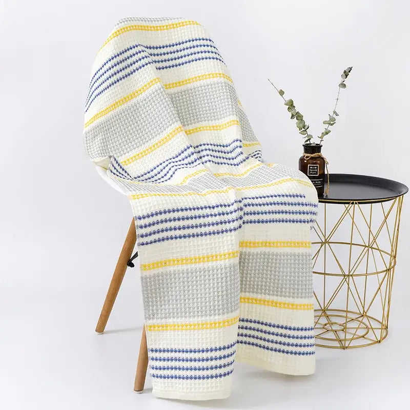 Cozy cream waffle-knit throw with yellow and navy stripes draped on chair complements decorbites cotton bath towel