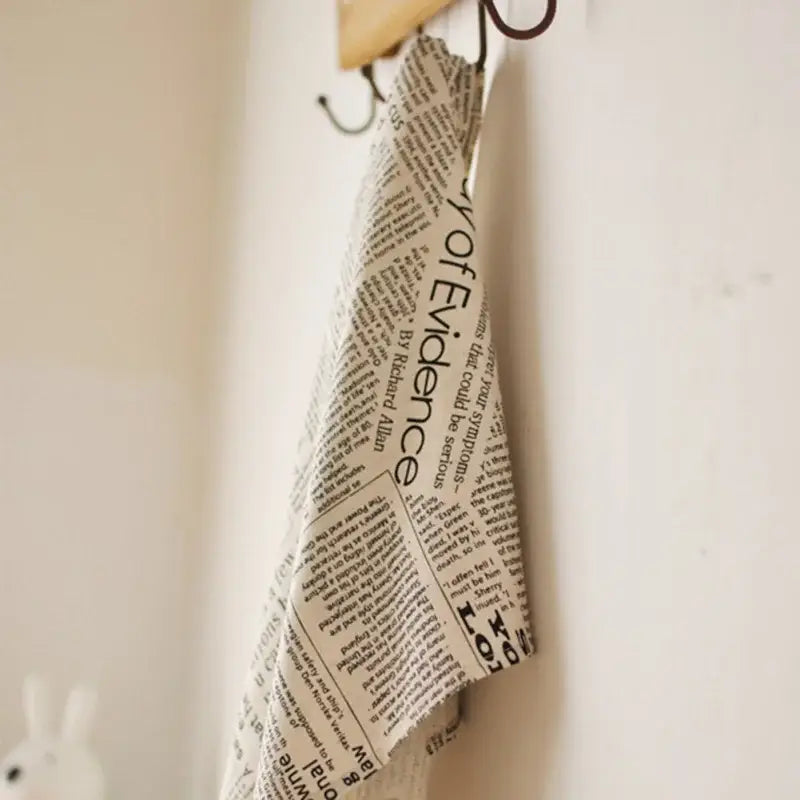 Beige newspaper style photography placemat with black text hanging from wooden hook ideal as english newspaper style props