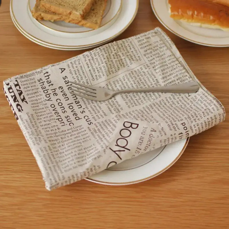 A beige newspaper style cloth napkin with black text folded on a plate as english newspaper style photography props