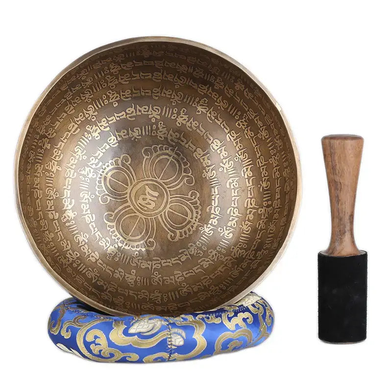 Brass engraved gold tibetan singing bowl with intricate sanskrit and floral design on ornate blue cushion for meditation
