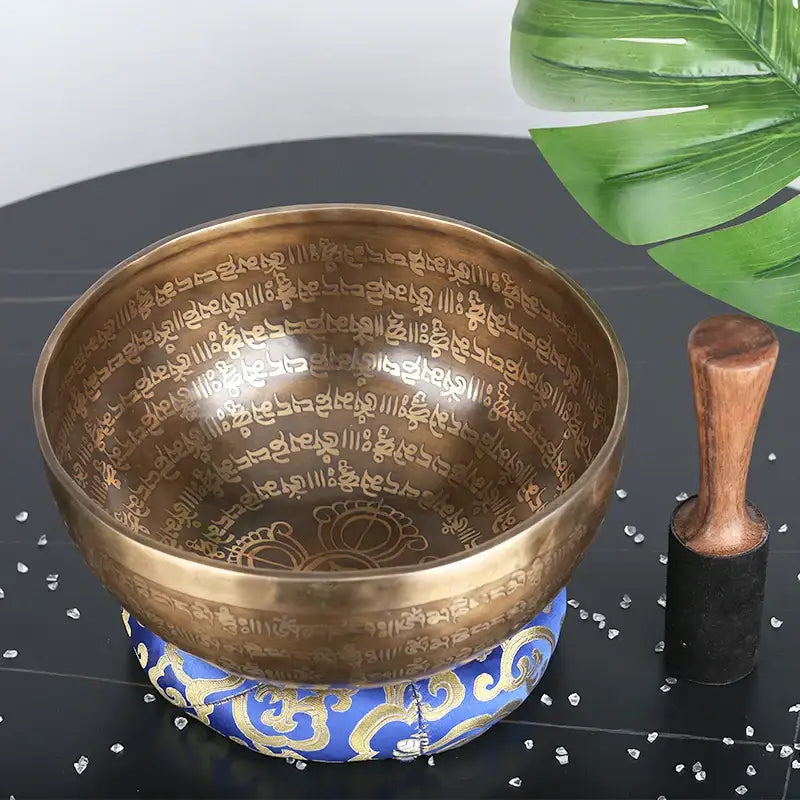 Engraved gold Tibetan singing bowl with intricate Sanskrit inscriptions and ornate blue base with wooden mallet for meditation