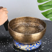 A golden engraved tibetan singing bowl with intricate script resting on a blue and gold patterned cushion