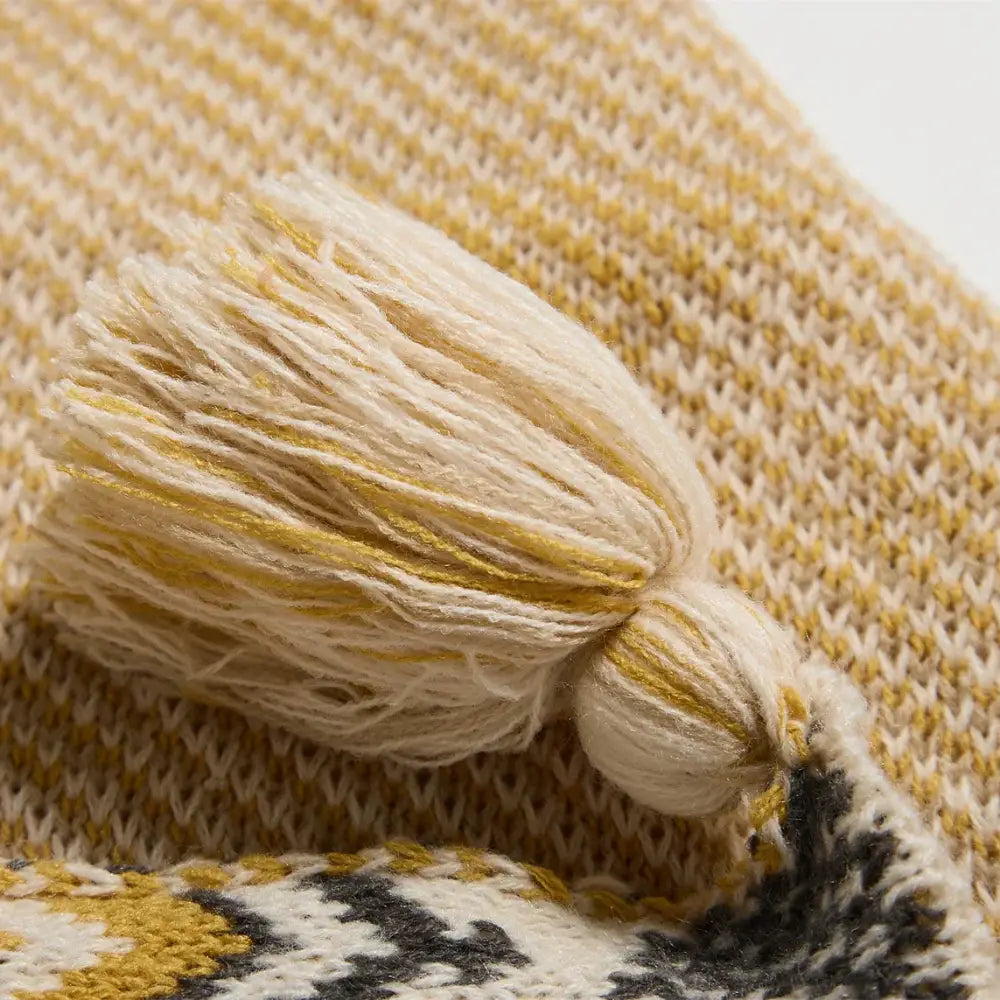 Ethnic bohemian blanket cream and gold knitted tassel resting on textured multicolored knit fabric decorbites ethnic