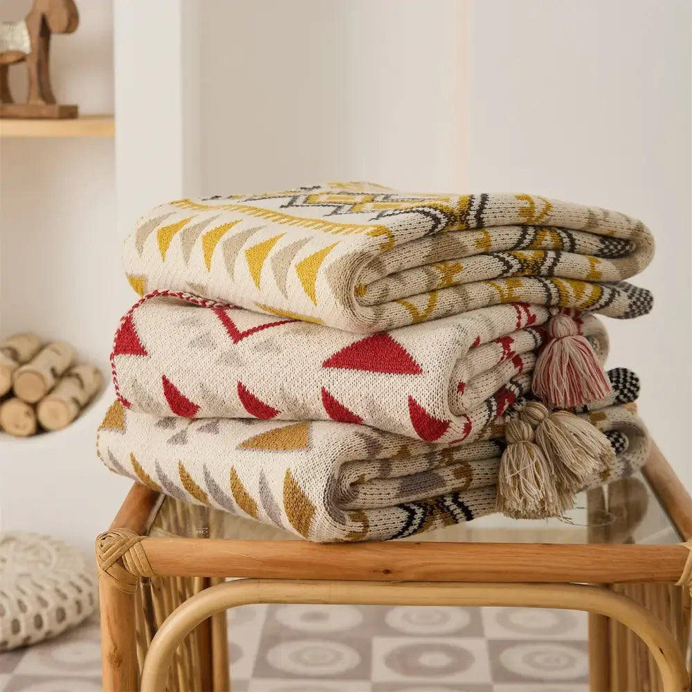 Stack of three decorbites ethnic bohemian knit throw blankets in cream, mustard, red, and black with tassels