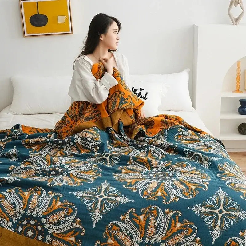 A cozy decorbites ethnic cotton blanket in teal and orange paisley draped over a woman sitting on a bed