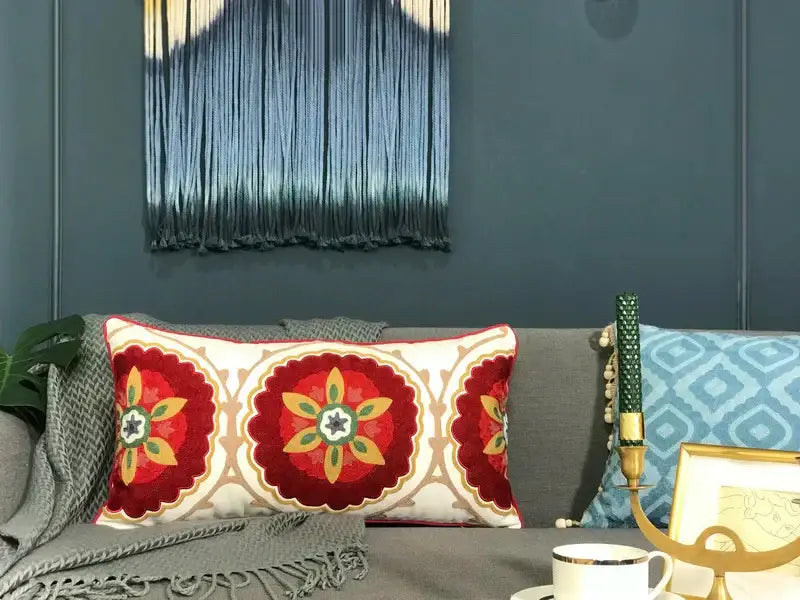 A cream rectangular pillow cover with intricate embroidered floral patterns in red yellow and beige ethnic tassels decor