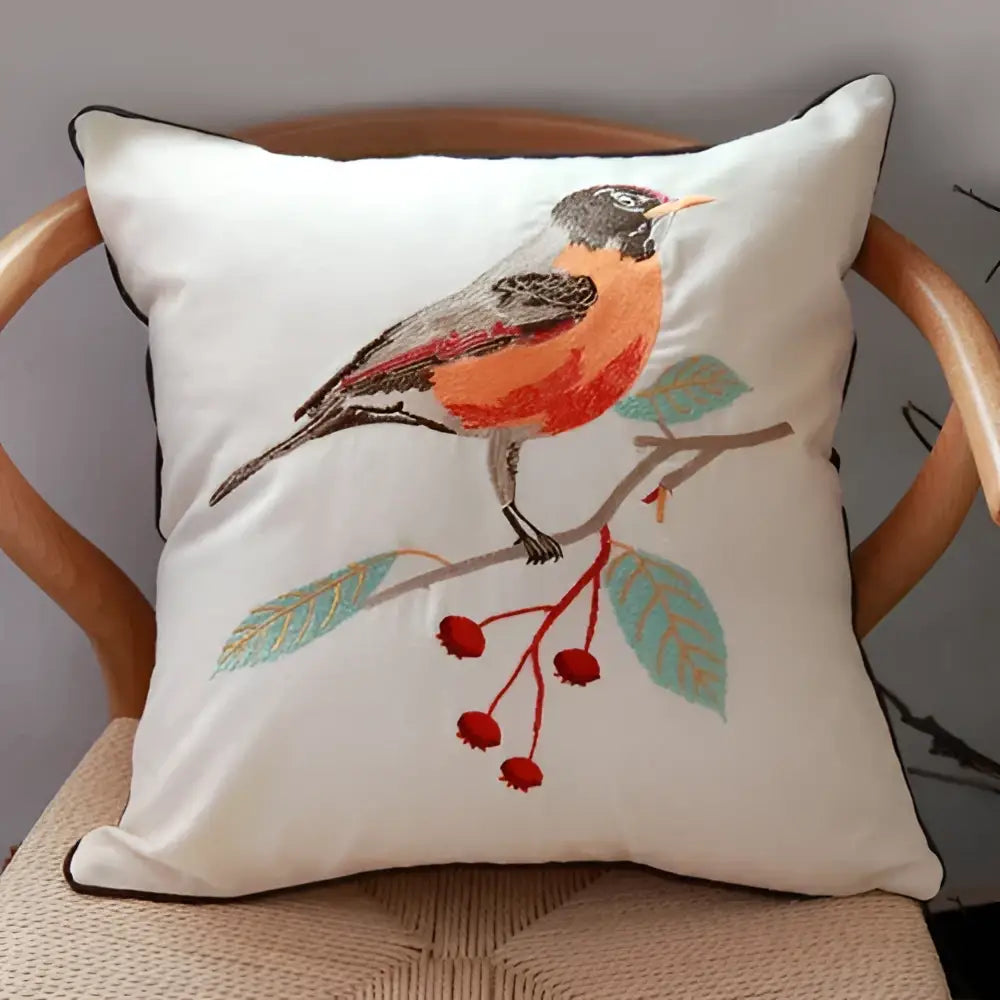 White cushion cover embroidered with a robin on a branch with red berries and teal leaves for sofa decor
