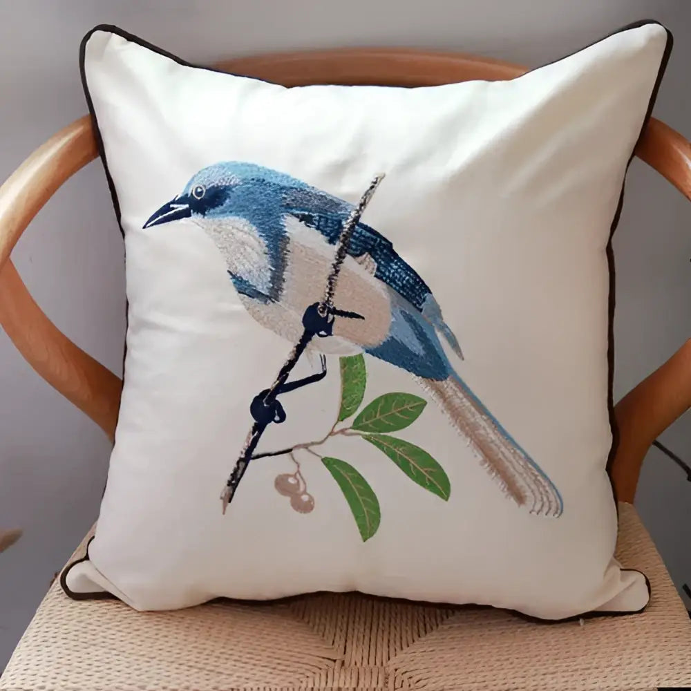 Cream-colored cushion cover with embroidered blue bird and green leaves framed by dark piping for sofa cushion cover