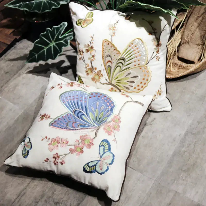 Two embroidered european cushion covers with butterfly and dragonfly designs on cream fabric with dark piping for sofa