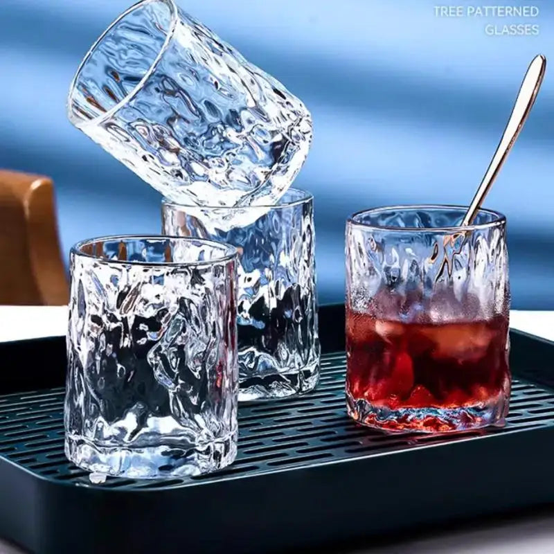 Clear tree-patterned glass tumblers with a hammered finish on a european gold deer glass storage rack with bamboo tray