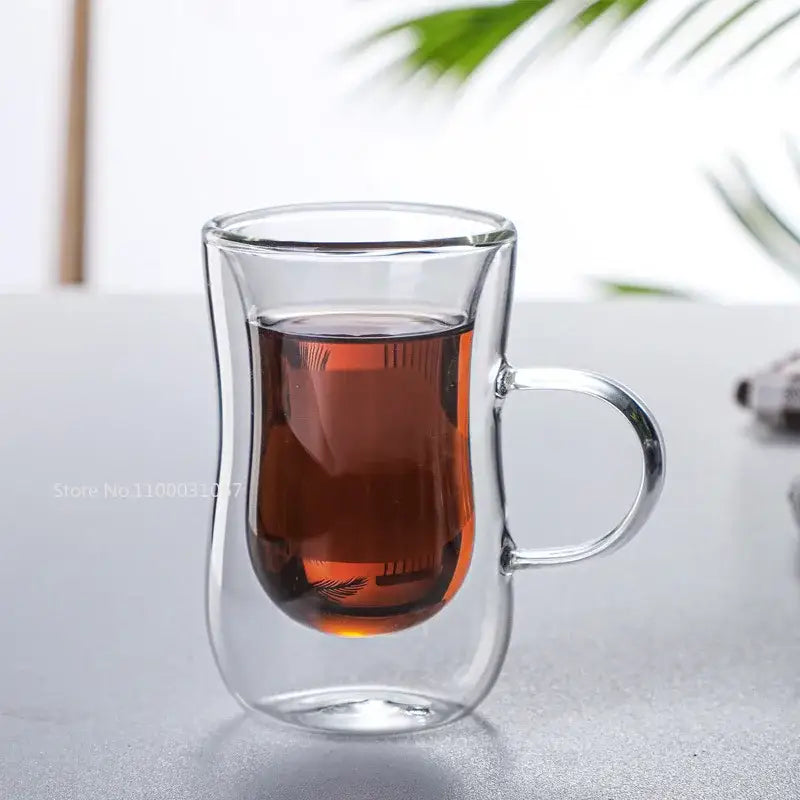 Clear double glass insulated tea cup filled with amber liquid featuring a handle for kitchenware use