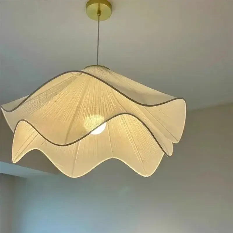 A cream-colored, wavy-edged fabric pendant light with a gold-toned ceiling mount.
