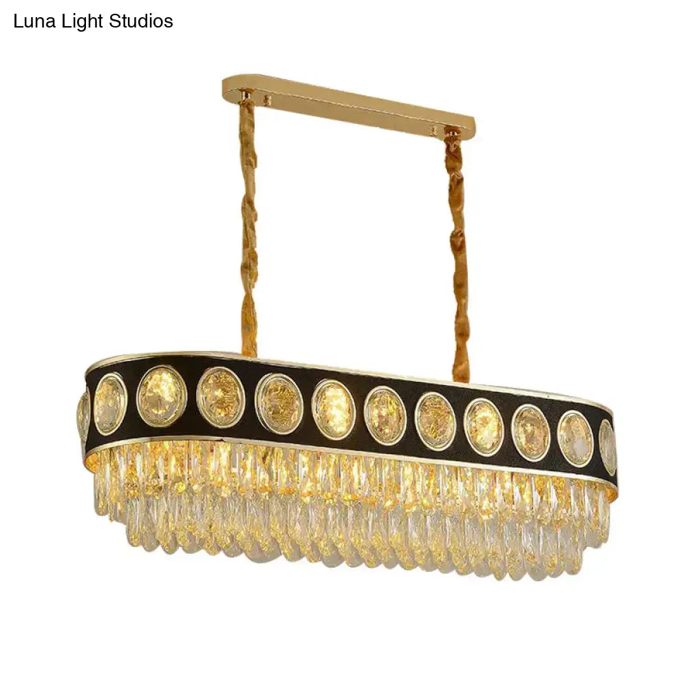 Gold-toned oval pendant light with black accent band featuring faceted crystal prisms and amber glass discs for dining room island