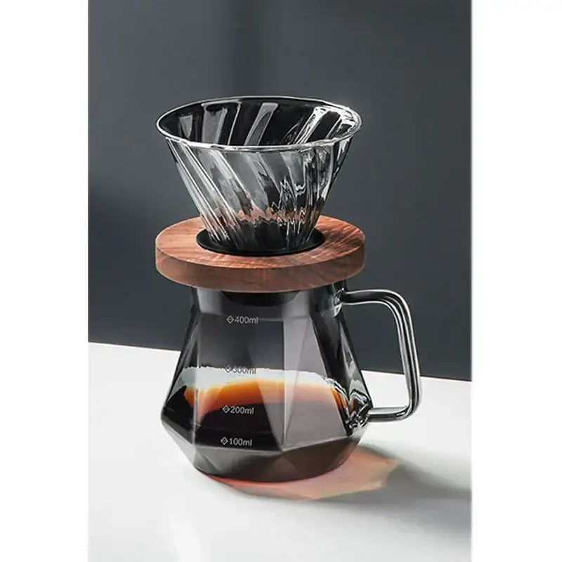 A sleek faceted dark tinted diamond glass coffee carafe with filter cup and wooden base for brewing coffee
