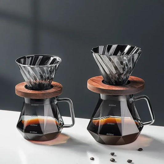Two elegant faceted dark tinted diamond glass coffee filter cup drippers with wooden lids atop matching glass coffee carafes