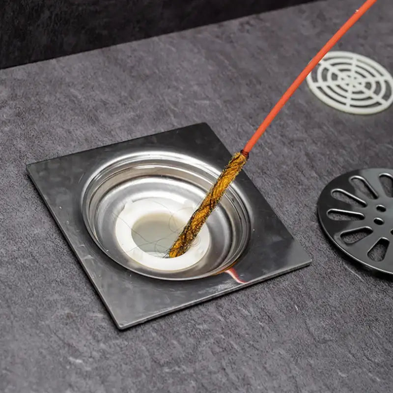 Orange incense stick with charred tip resting in stainless steel drain illustrating flexible drain cleaner brush use