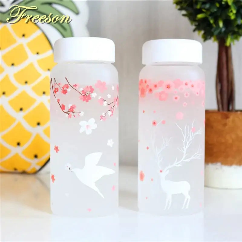 Two frosted glass water bottles with white lids featuring pink cherry blossoms and floral elk designs for kitchen use