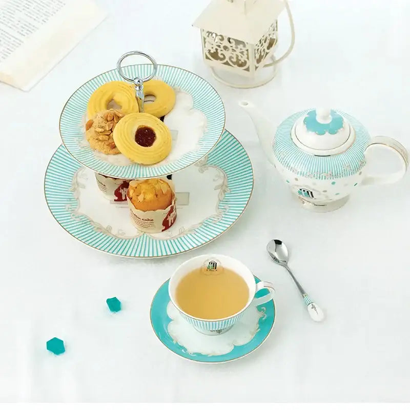 A delicate turquoise and white floral bone china tea set two-tiered serving tray with gold trim holding assorted pastries