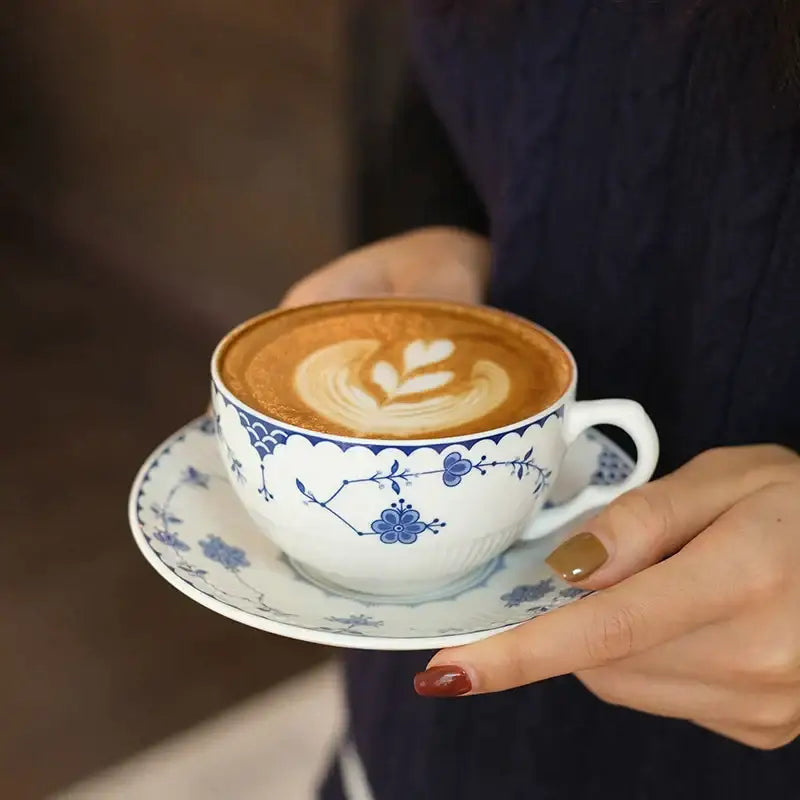 A white ceramic teacup with blue floral patterns and scalloped rim on a matching saucer for decorbites ceramic dinner plate set