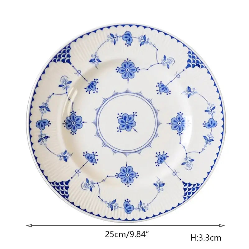 A white ceramic dinner plate with intricate blue floral and vine patterns and scalloped fish-scale rim decorbites ceramic dinner