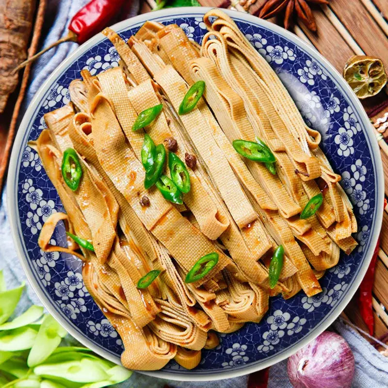 A floral blue and white porcelain serving plate with marinated tofu skin strips garnished with sliced green chilies