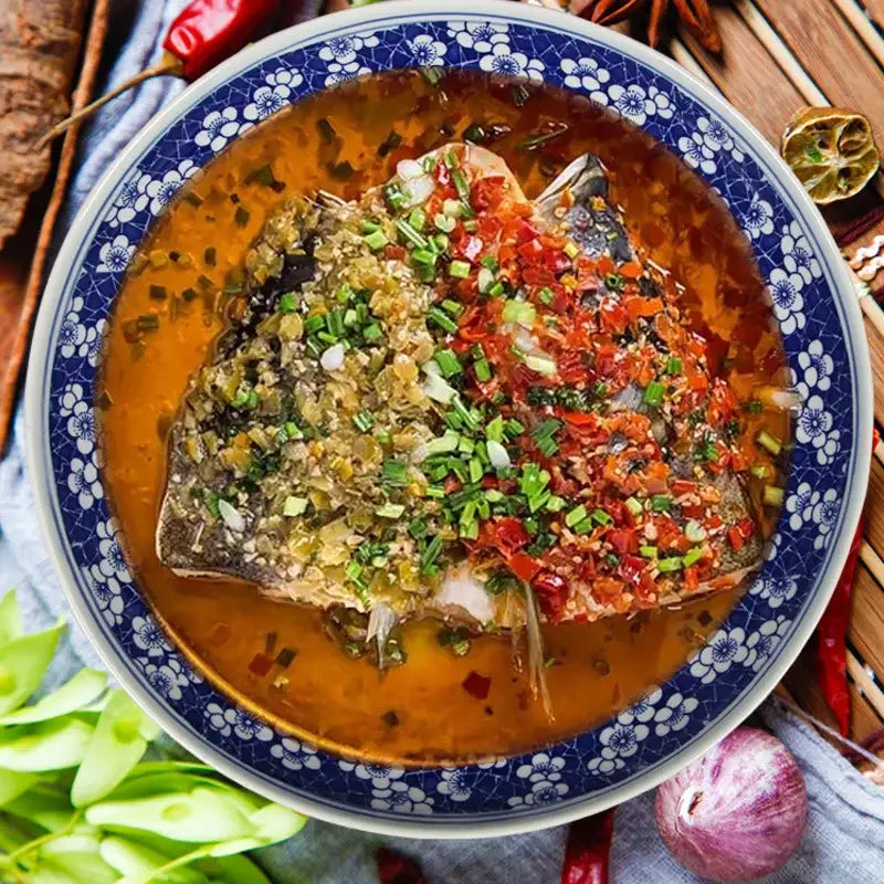 A whole fish in savory sauce on a floral blue and white white porcelain serving plate with green onions and chili flakes