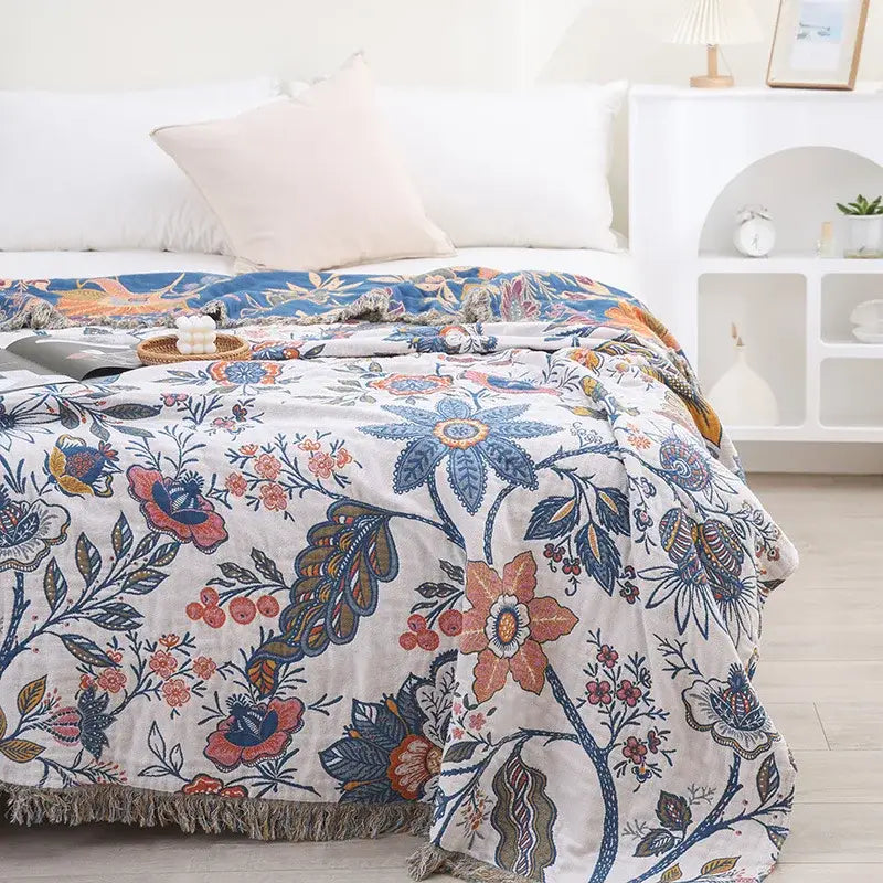 A double cotton bohemian throw blanket in off-white with vibrant blue orange and pink floral patterns and fringed edges